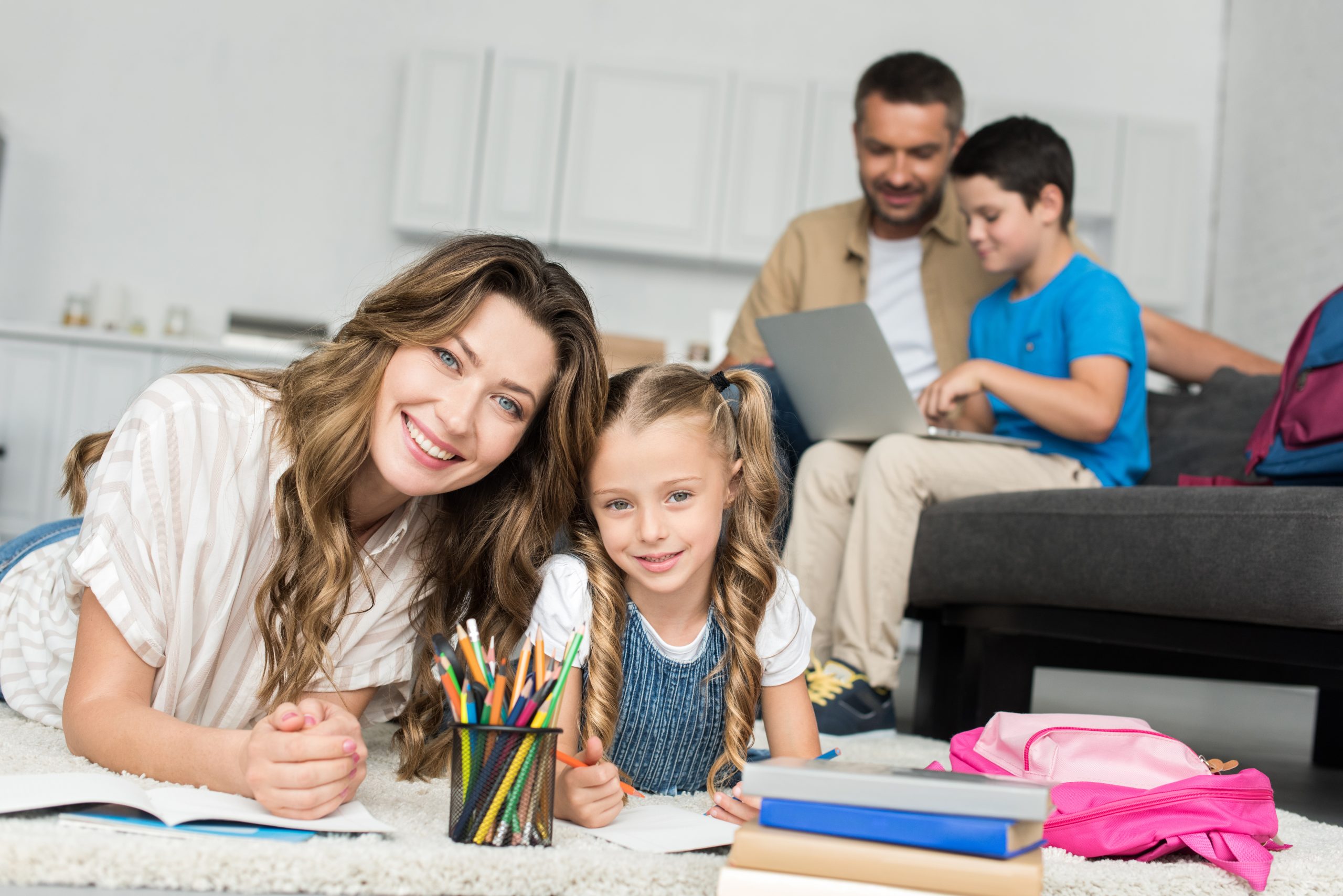 selective focus of smiling mother and daughter doing homework while father and son using laptop on