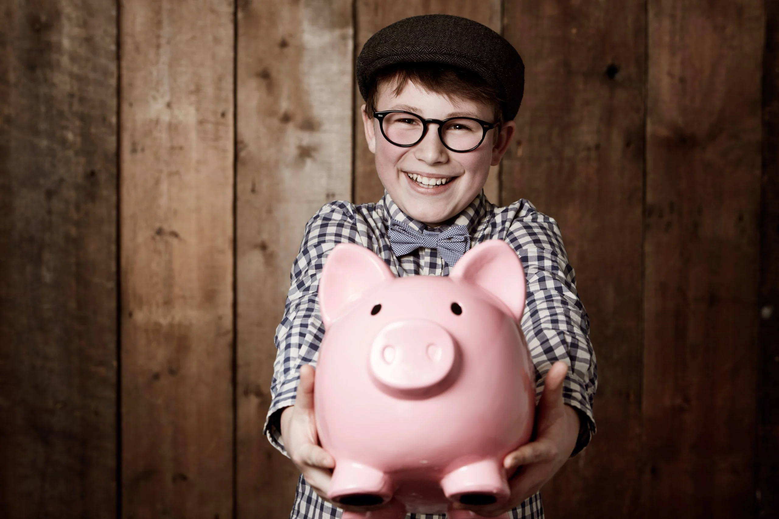 Uśmiechnięty chłopiec w okularach trzymający różową skarbonkę – edukacja finansowa i oszczędzanie z kontem bankowym dla dzieci