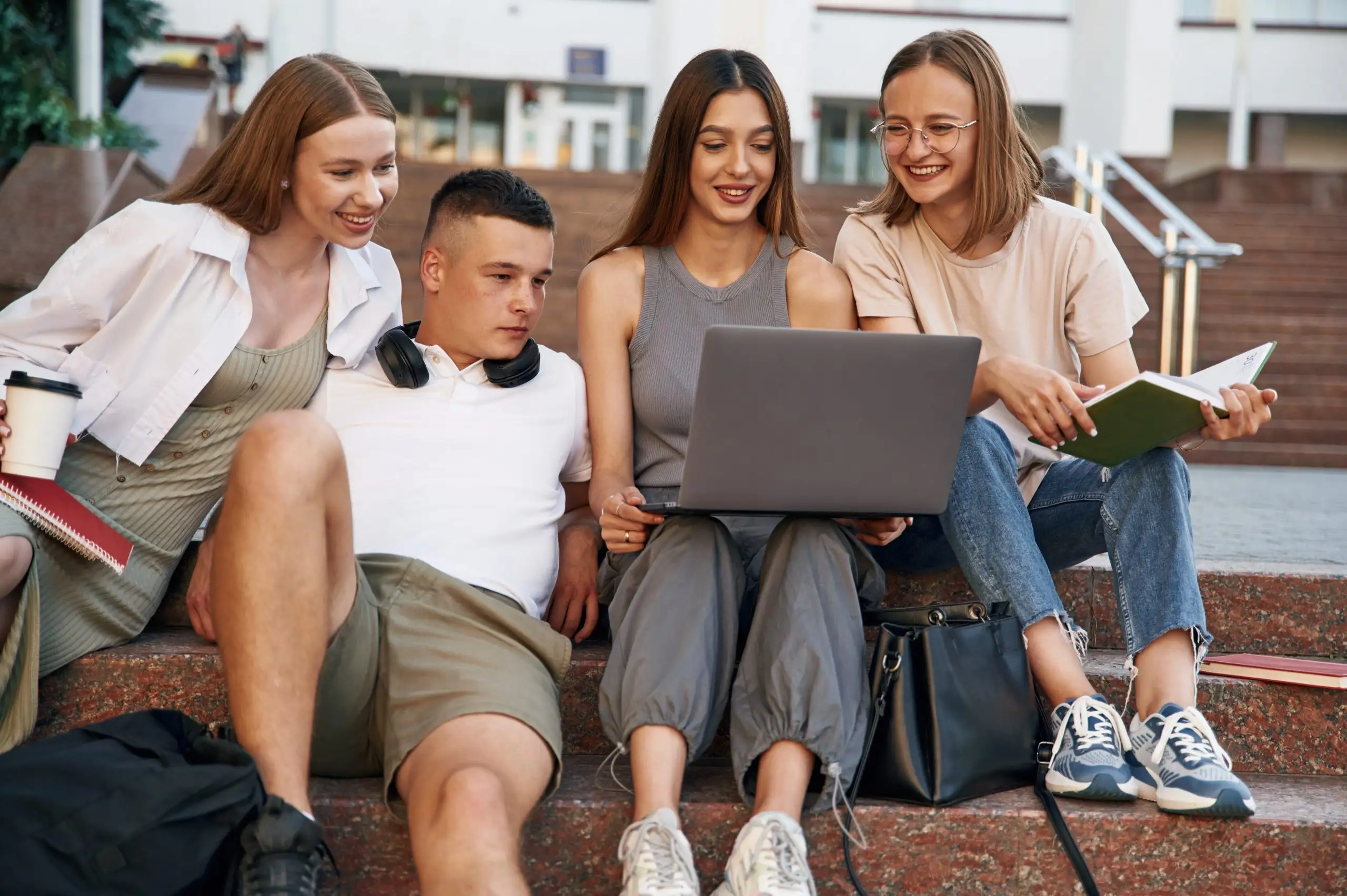 Młodzi ludzie siedzący na schodach z laptopem i książkami – oferta konta młodzieżowego z bankowością internetową