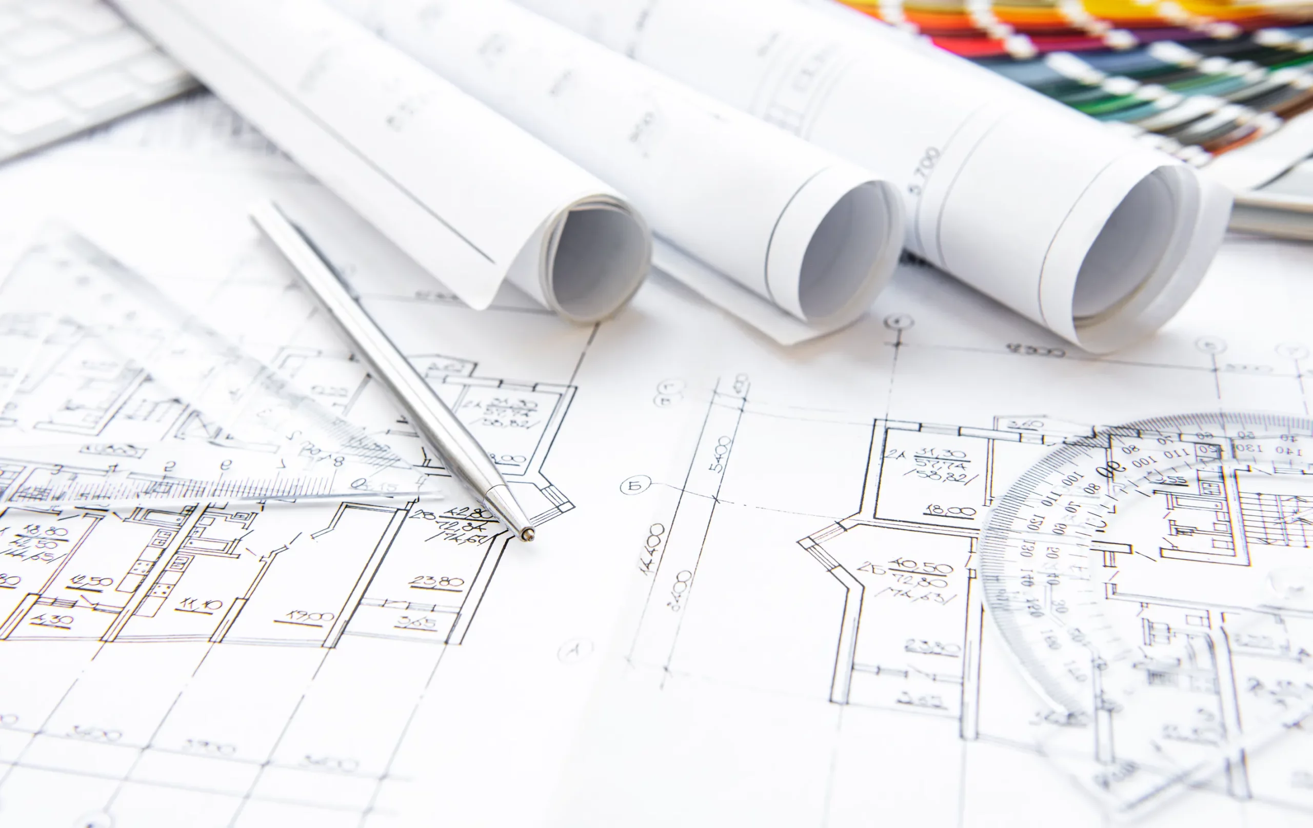 Rozłożone plany architektoniczne z przyrządami kreślarskimi i zwiniętymi projektami budowlanymi.