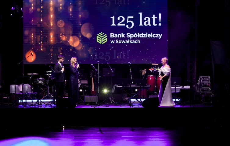 Prowadzący galę jubileuszową oraz Prezes Banku Spółdzielczego w Suwałkach stoją na scenie przed dużym ekranem z napisem „125 lat!”, podczas uroczystości 125-lecia banku.