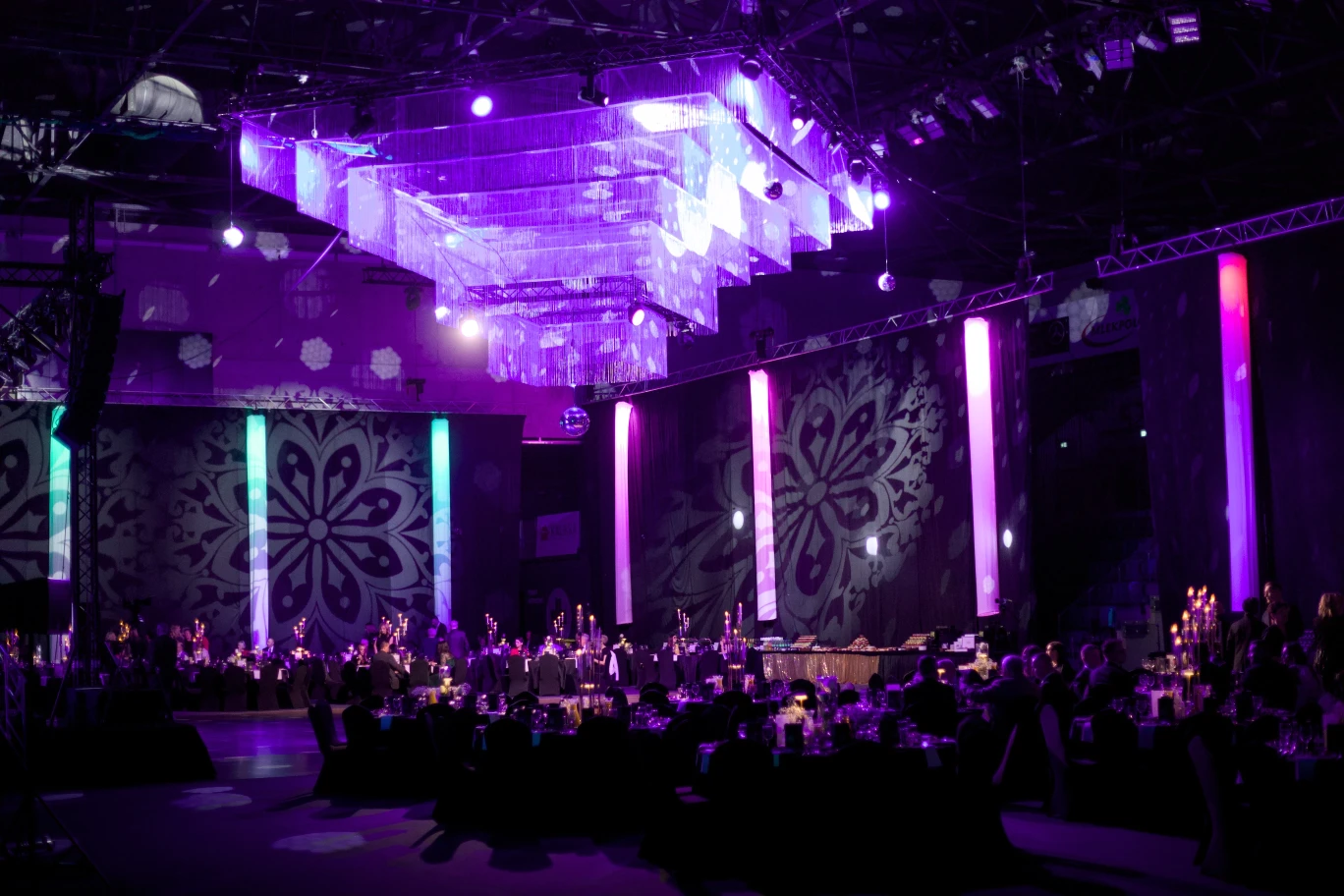 Sala bankietowa podczas gali 125-lecia Banku Spółdzielczego w Suwałkach, z dużym podświetlanym żyrandolem, udekorowanymi stołami i gośćmi siedzącymi przy nakryciach.