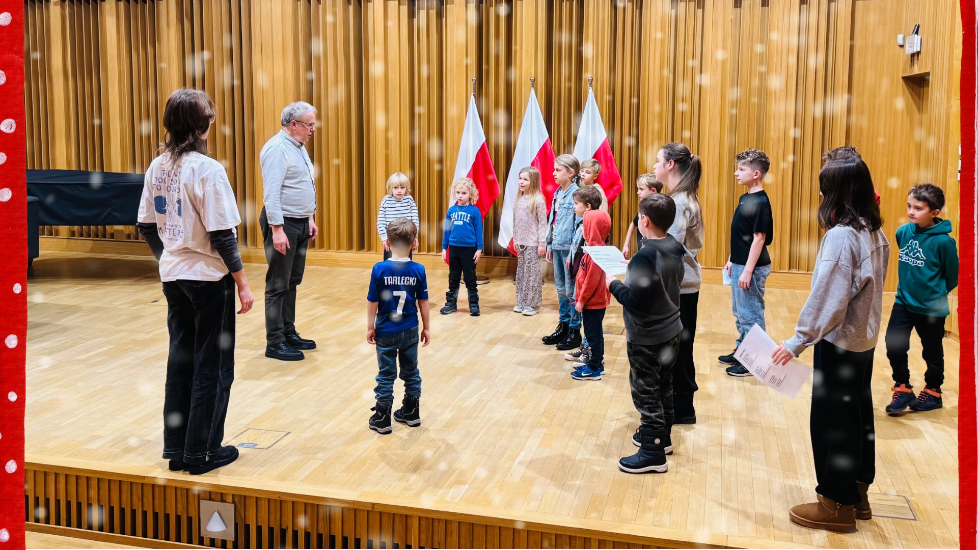 Grupa dzieci stojących w kole podczas próby kolęd w sali koncertowej.